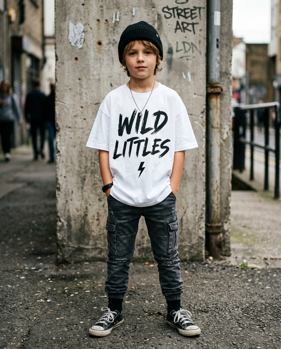 Kid wearing oversized white Wild Littles Core Logo Tee with black brush-script graphic and lightning bolt