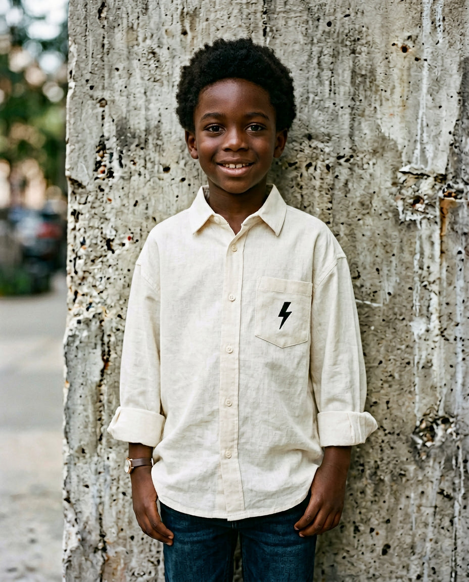 Black boy wearing cream linen button-up shirt with embroidered Wild Littles lightning bolt on the chest pocket