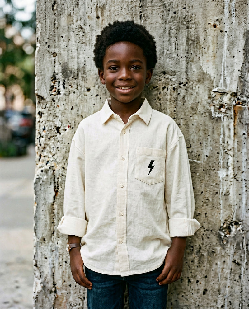 Black boy wearing cream linen button-up shirt with embroidered Wild Littles lightning bolt on the chest pocket